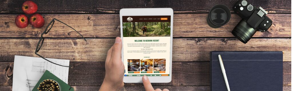 Person holding a tablet displaying a resort website on a wooden desk, representing how optimized lodging websites can drive guest engagement and increase direct bookings.