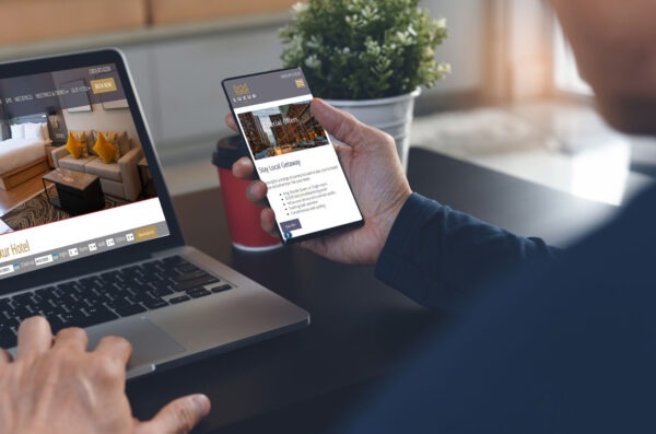 Person on phone and computer looking at hotel website.